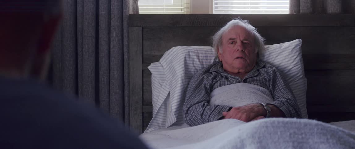 Medical professional sits to talk with elderly patient lying down in bed at home