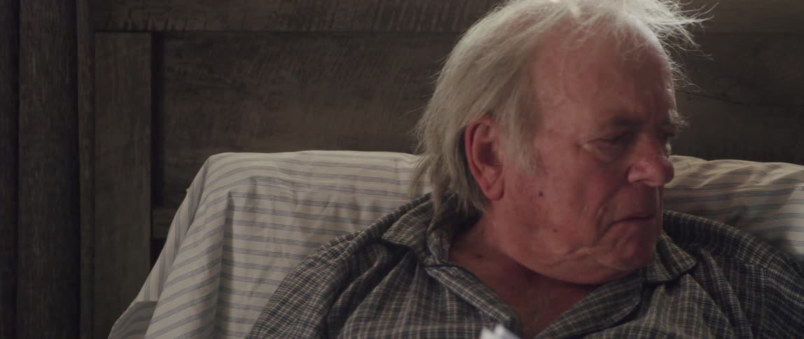 Elderly man resting in bed puts on glasses to read a brochure