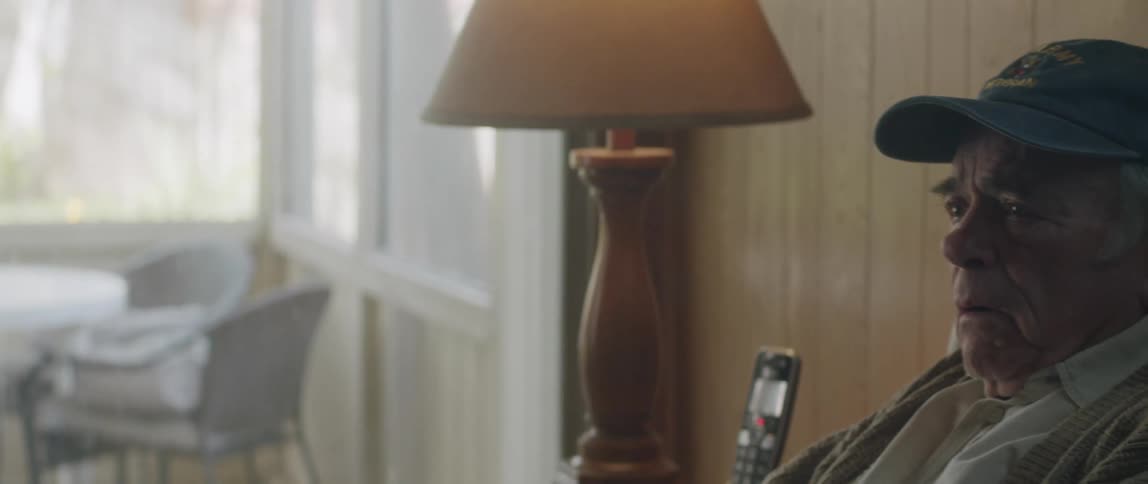 An old man speaks to another man in a living room