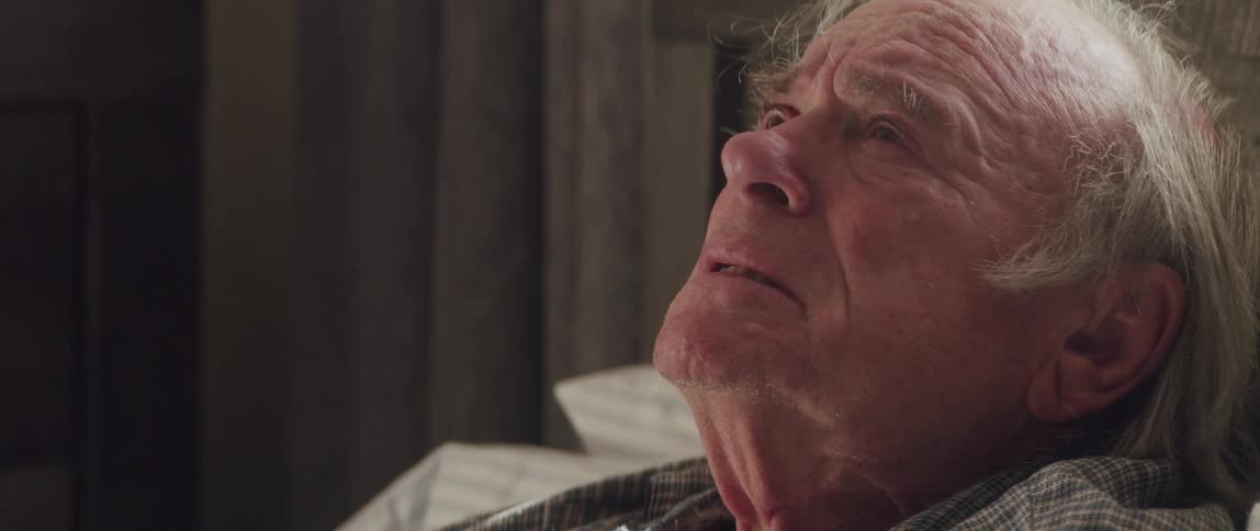 An older man coughs and takes a deep breath before crying and sinking into his bed