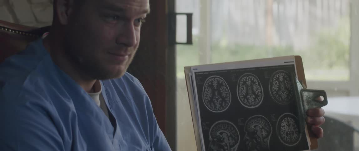 A doctor sitting in a chair holding a pen and a chart with a brain exam explaining the exam to someone