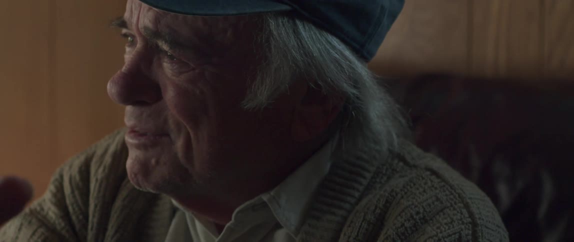 The face of an elderly man with a cap and he is talking to someone