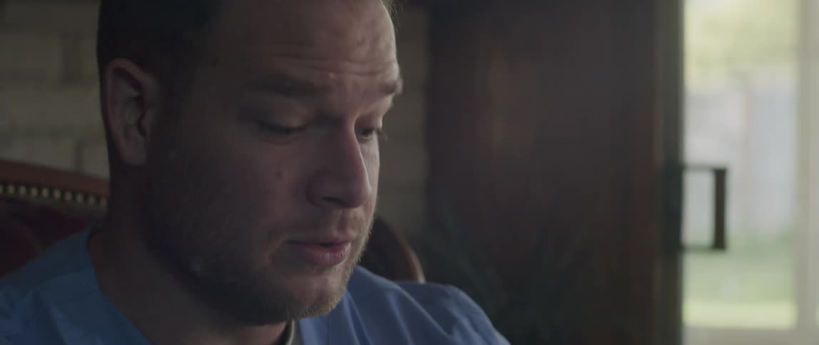 A man wearing scrubs is holding open a medical brochure and showing it to someone he is talking to out of view