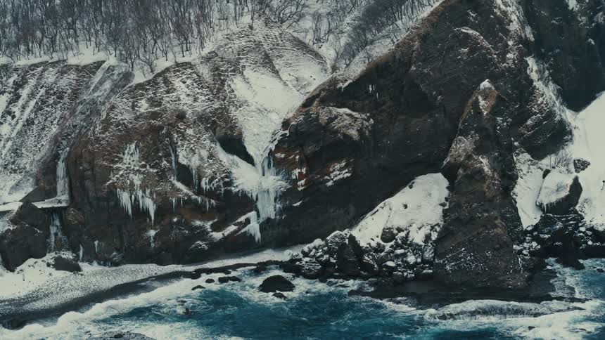 Aerial panorama of a crystal blue sea with waves crashing on the shore covered in snow