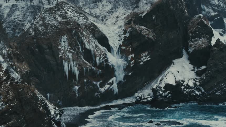 Aerial landscape with blue sea crashing on rocky shore covered by snow