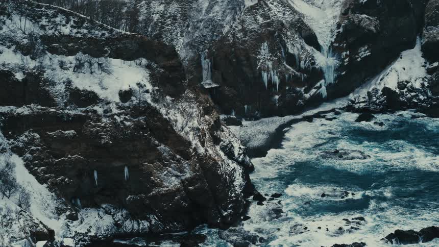Aerial panorama of the sea and surrounding mountains covered in snow on a rainy day