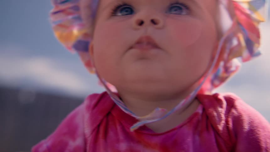 Baby balances with help from an adult while sitting in a fencedin yard