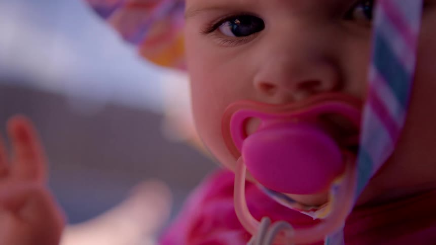 A person lifts a hat off of a baby sucking on a pacifier