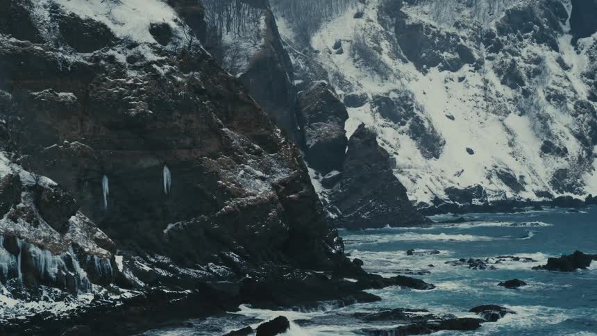 Black snowcapped rocky mountains on the edge of a clear blue sea