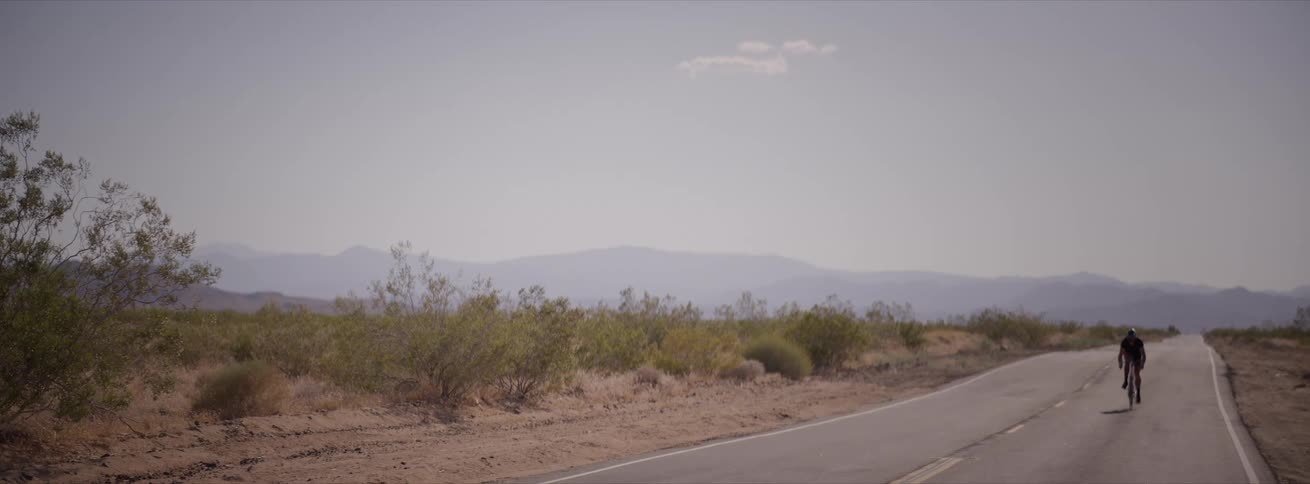 Man cycling on a highway in a desert environment on a blue sky day with few clouds