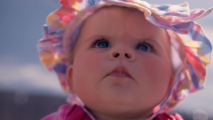 Portrait of a blueeyed baby girl with a small hat and sun glare