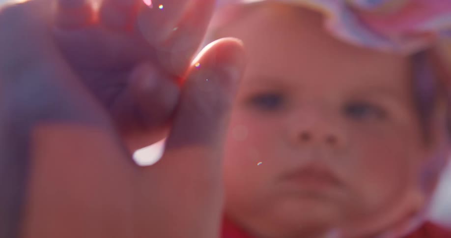 Portrait of a baby with light eyes holding someone elses hands with her little hands