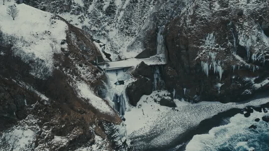 Aerial landscape of a blue sea arriving at the mountainous coast on a snowy day