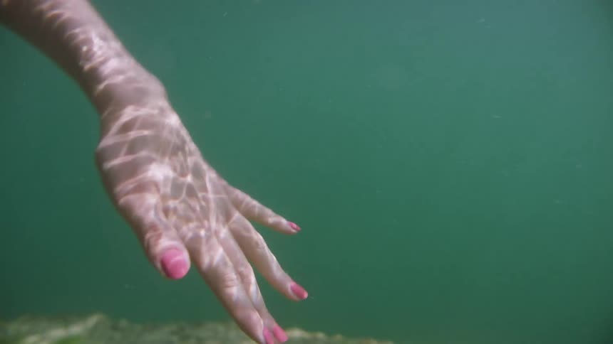 A female hand underwater with red nail polish on the fingernails