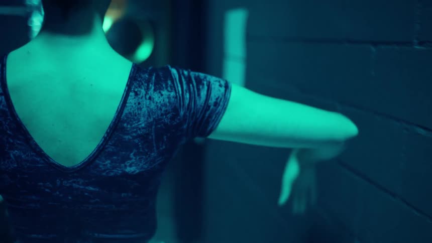 A ballet dancer moves her arms and hands up and down back stage as she dances toward a dressing room