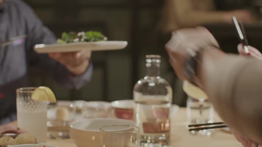 Hands of people at a table helping themselves to a table with drinks and food