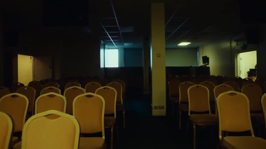 An empty and dimly lit conference or meeting room with aligned yellow chairs