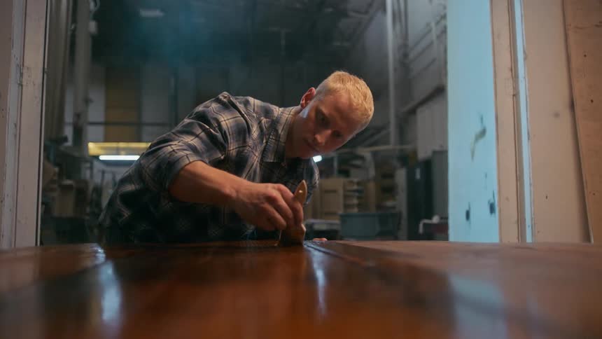 Carpenter man applying varnish to a bottle using a brush