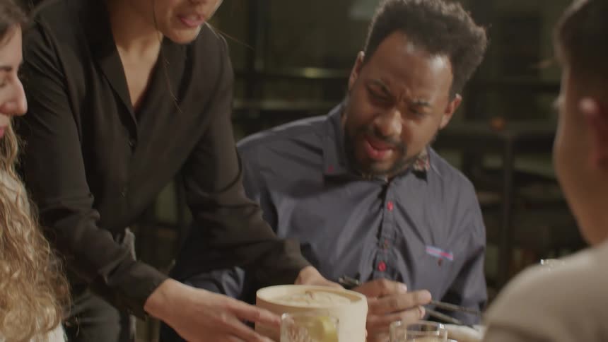 A waiter serving dumplings at a table with friends