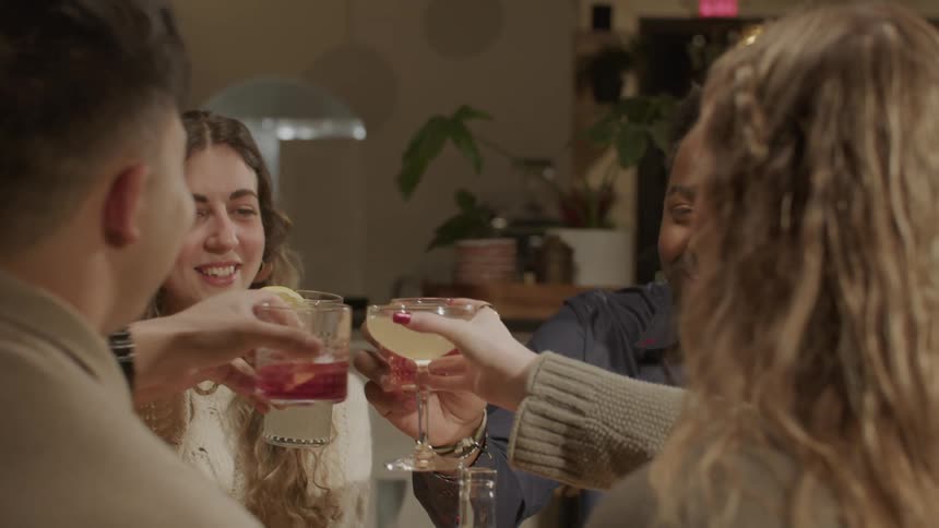 Couples of friends sitting at a table toasting and having their drinks in a bar at night