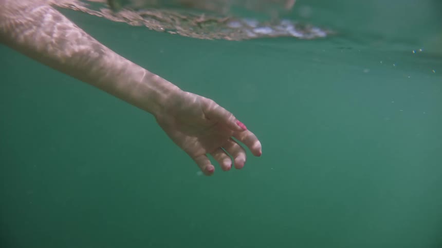 Inside the clear and crystalline sea with solar reflections a womans hand is swimming