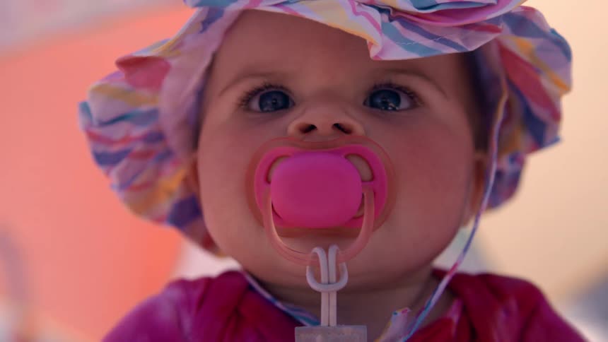Close up of the face of a baby wearing colorful clothes and pacifier