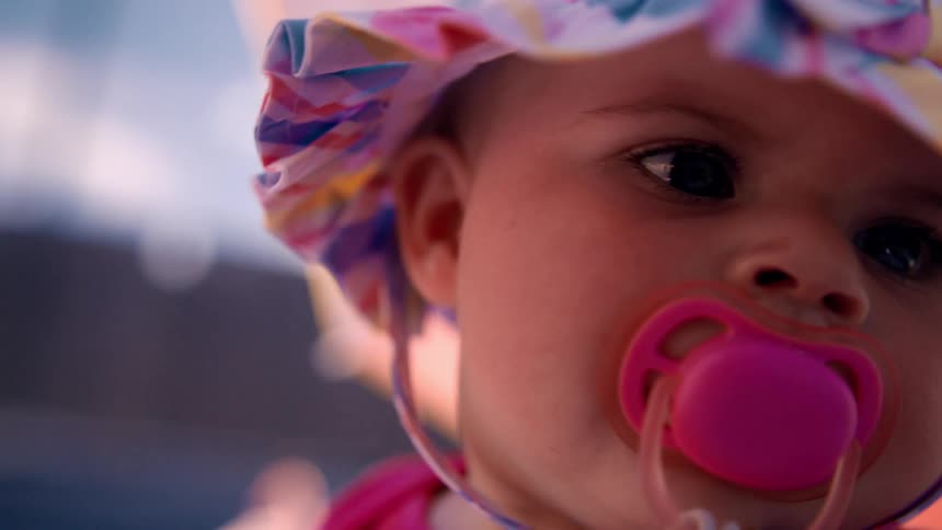 Close up of the face of a baby wearing colorful clothes and pacifier