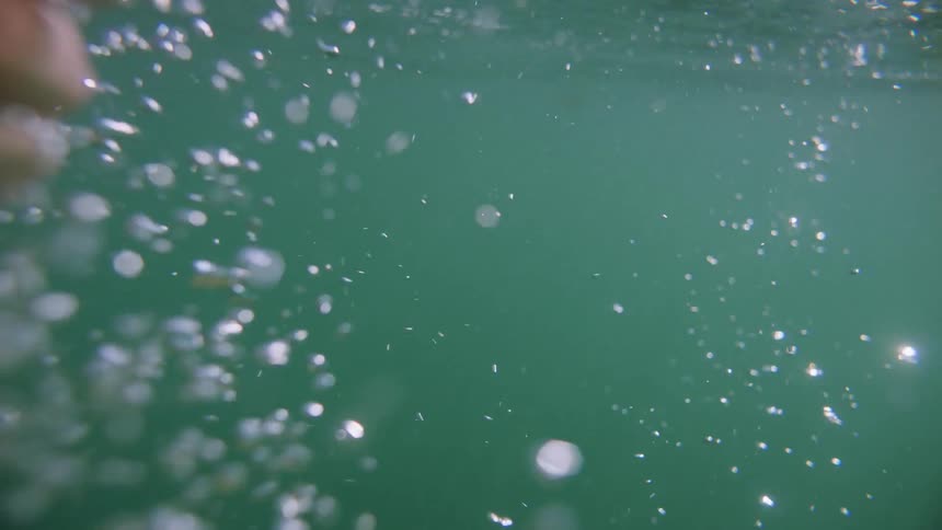 A womans hand in a crystal clear sea with sunlight