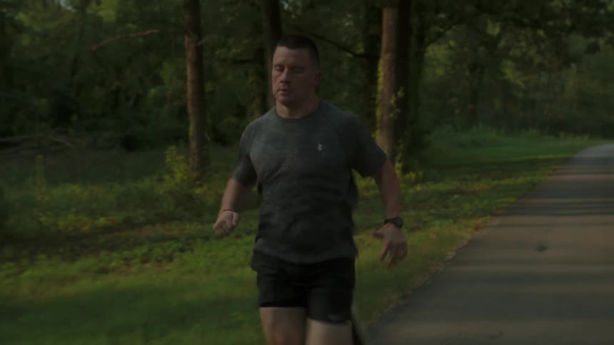 A person jogging on a paved path surrounded by lush forests