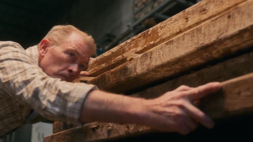 Woodworker examines a rough plank of wood by looking down from one end to the other