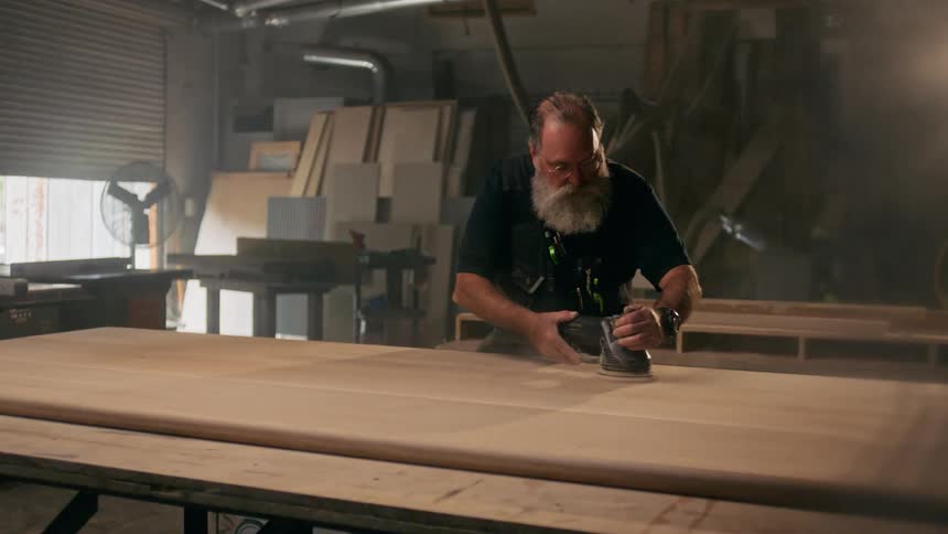 Man indoors with the help of a machine polishing a wooden sheet