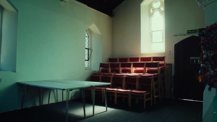 Room inside a church with tables and chairs stored next to windows with solar reflection