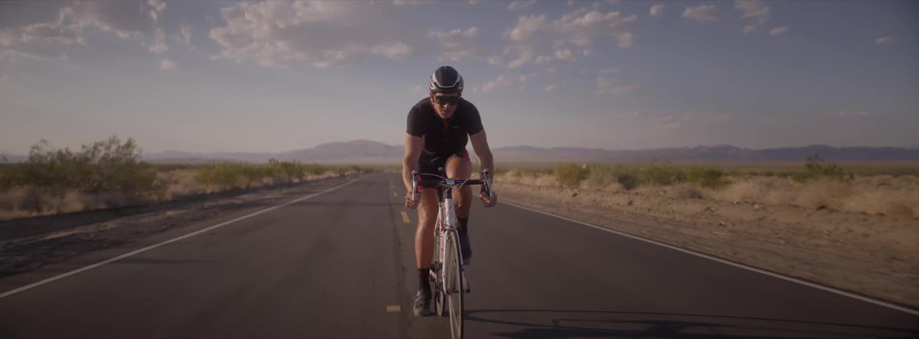 A man rides his bicycle on a rural road with mountains in the distance