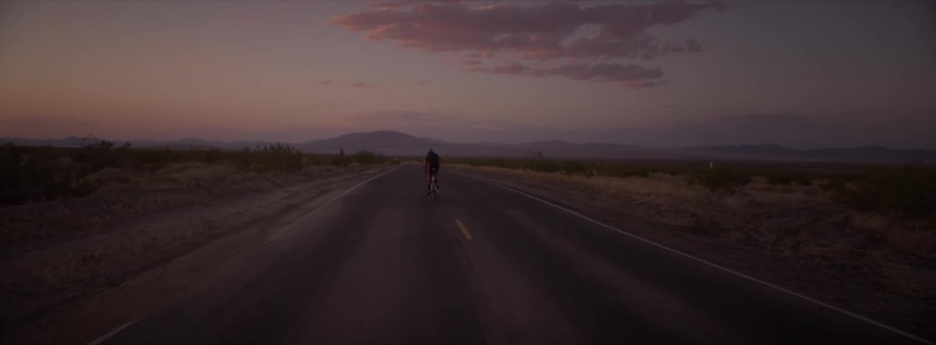 Cyclist cycling on a street in a desert location on a morning with a purple sky