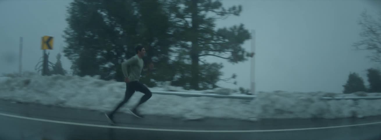 A person running on a road beside a snowy landscape with an overcast