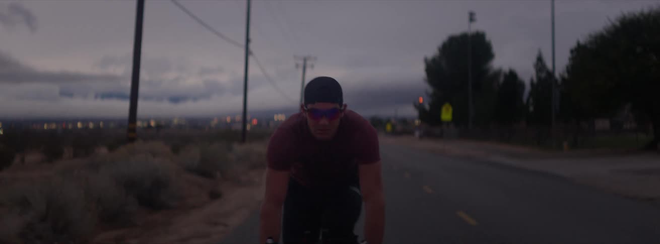 A person driving a bicycle on a road near a field during dusk