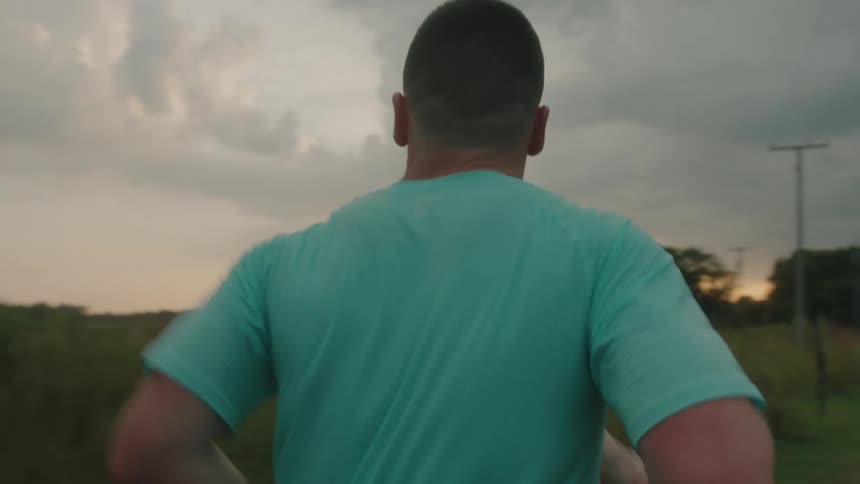 A man is jogging near a field as he runs to the main road