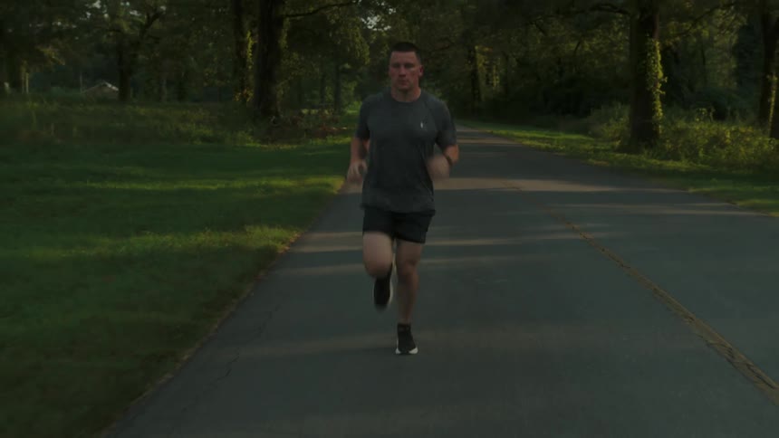 A man jogging on a road across a park