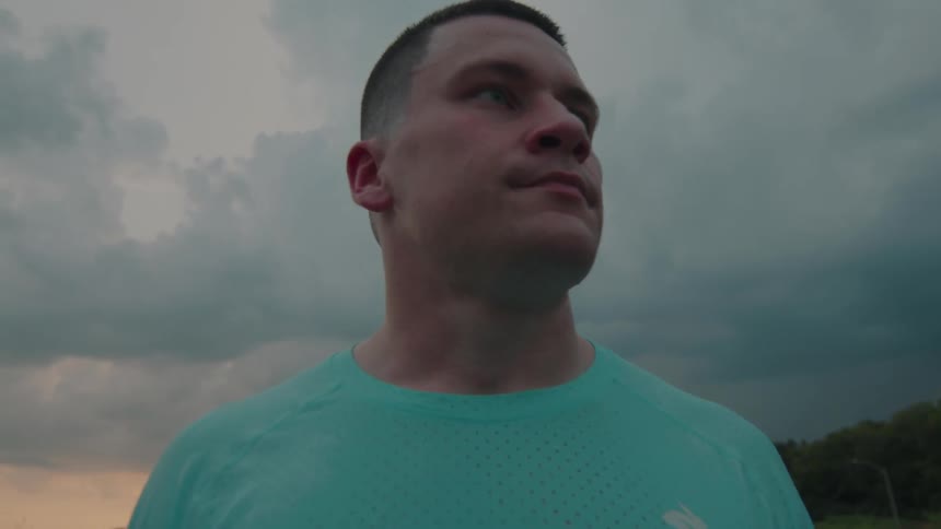 Man in workout clothes walks on a path through a grassy field at sunset