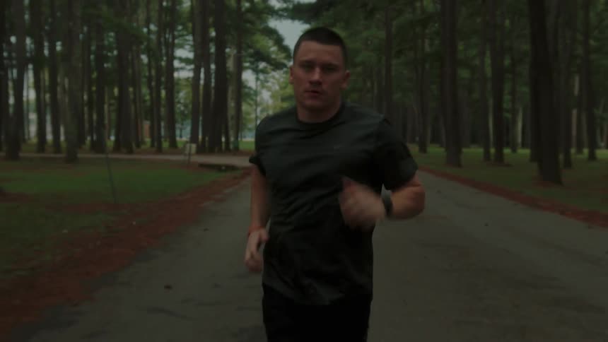 A man is jogging on a road through a park filled with trees