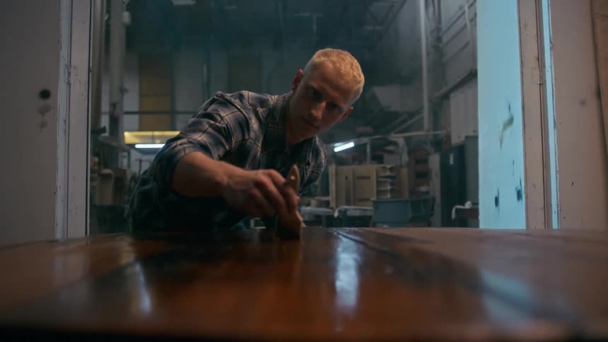 A man carefully varnishing a wooden table