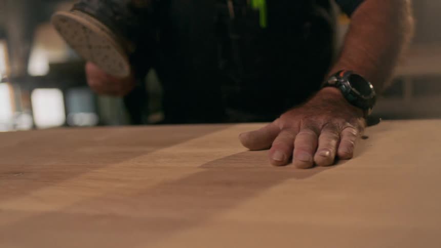 A man runs his hand over a freshly sanded table