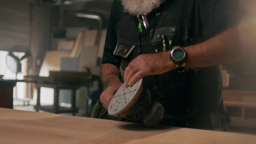 Woodworker examines his orbital sander in his workshop