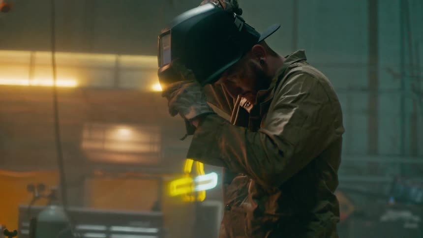 Man inside a factory putting on a protective welding helmet and picking up machinery