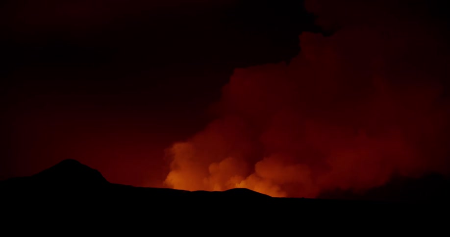 Glowing red smoke fills the sky and rises over mountains