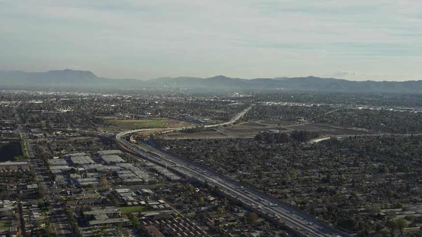 Busy freeway winds through city bordering mountains on a foggy day