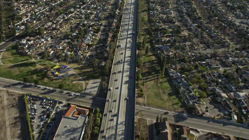 Cars drive down a highway surrounded by suburbs