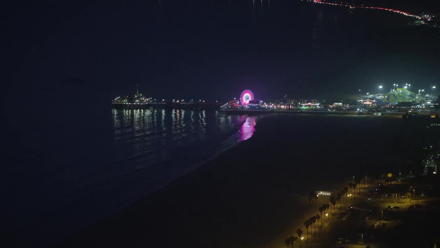 A long pier has a brightly illuminated ferris wheel spinning atop it