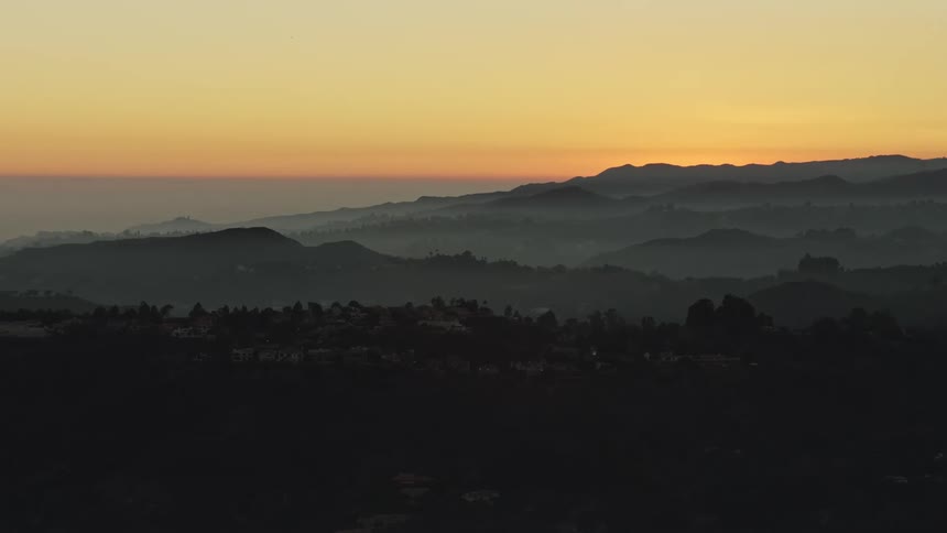 Aerial landscape of hills and mountains with some houses and orange sky