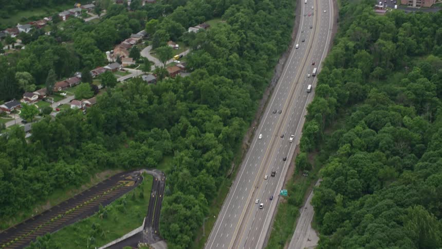 Aerial view of a highway with vehicles surrounded by greenery and residential buildings